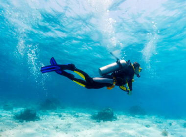 A scuba diver with good buoyancy and trim, diving over a sandy bottom.