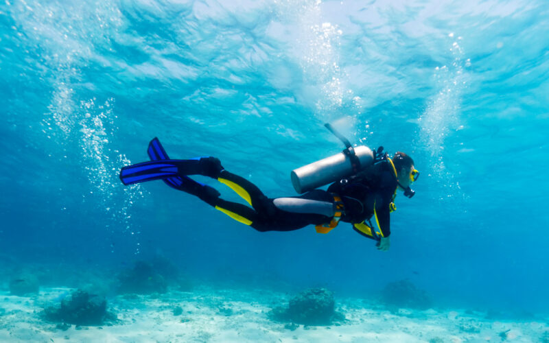 A scuba diver with good buoyancy and trim, diving over a sandy bottom.