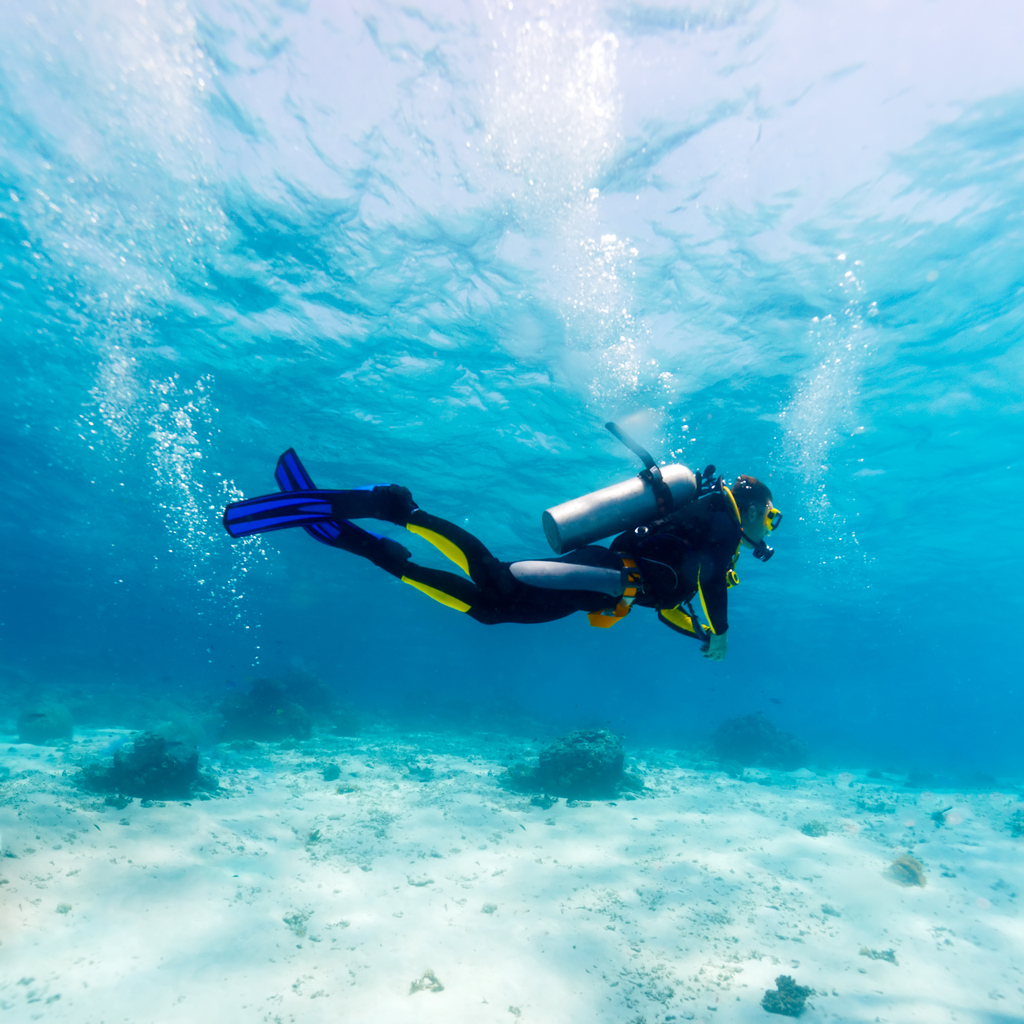 A scuba diver with good buoyancy and trim, diving over a sandy bottom.