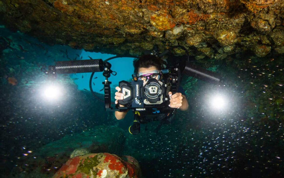 A diver holding a smartphone in a DiveVolk SeaTouch underwater housing on a coral reef