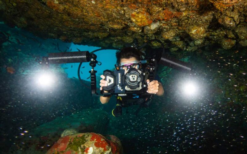 A diver holding a smartphone in a DiveVolk SeaTouch underwater housing on a coral reef