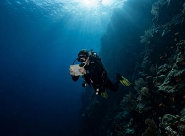 Scuba diver checking dive computer at depth along a deep blue drop-off wall