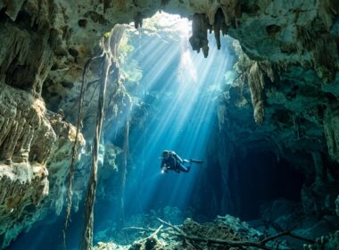 Diver in cenote with sunlight beams and limestone formations underwater